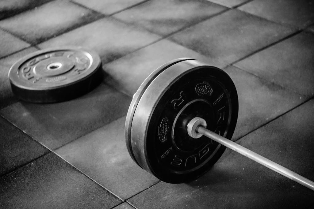 Grayscale image of heavy gym barbell and weights on rubber mat flooring.